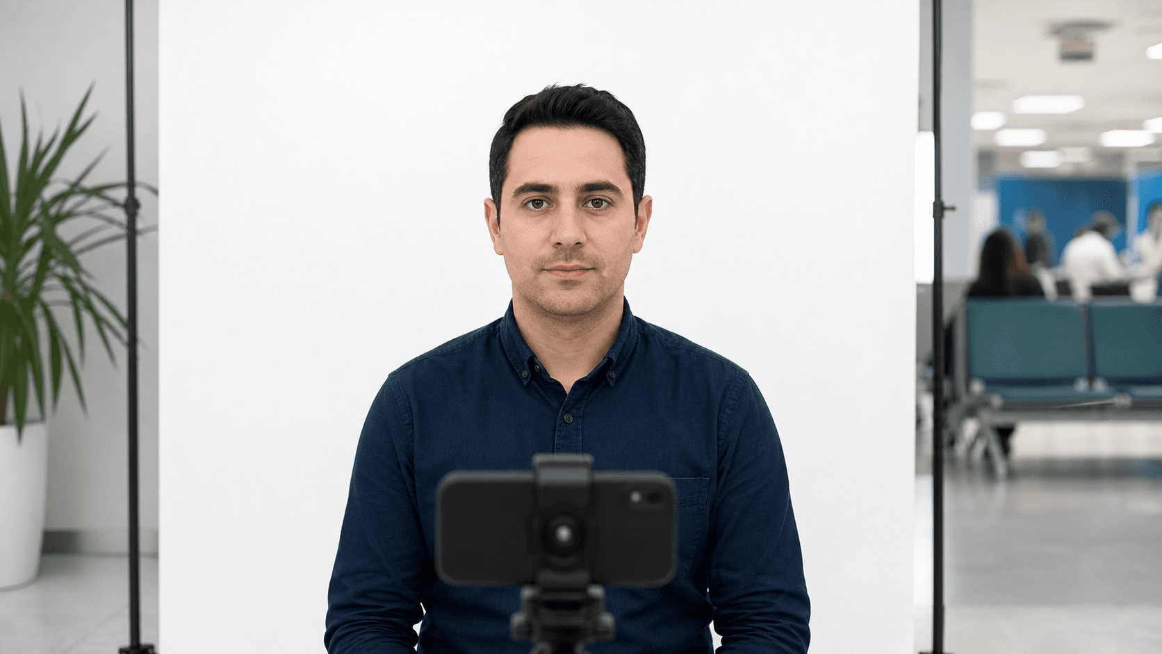 T.C. kimlik kartı yenilemesi için beyaz fonda göz hizasındaki telefonla nötr ifadeli biyometrik fotoğraf çeken yetişkin