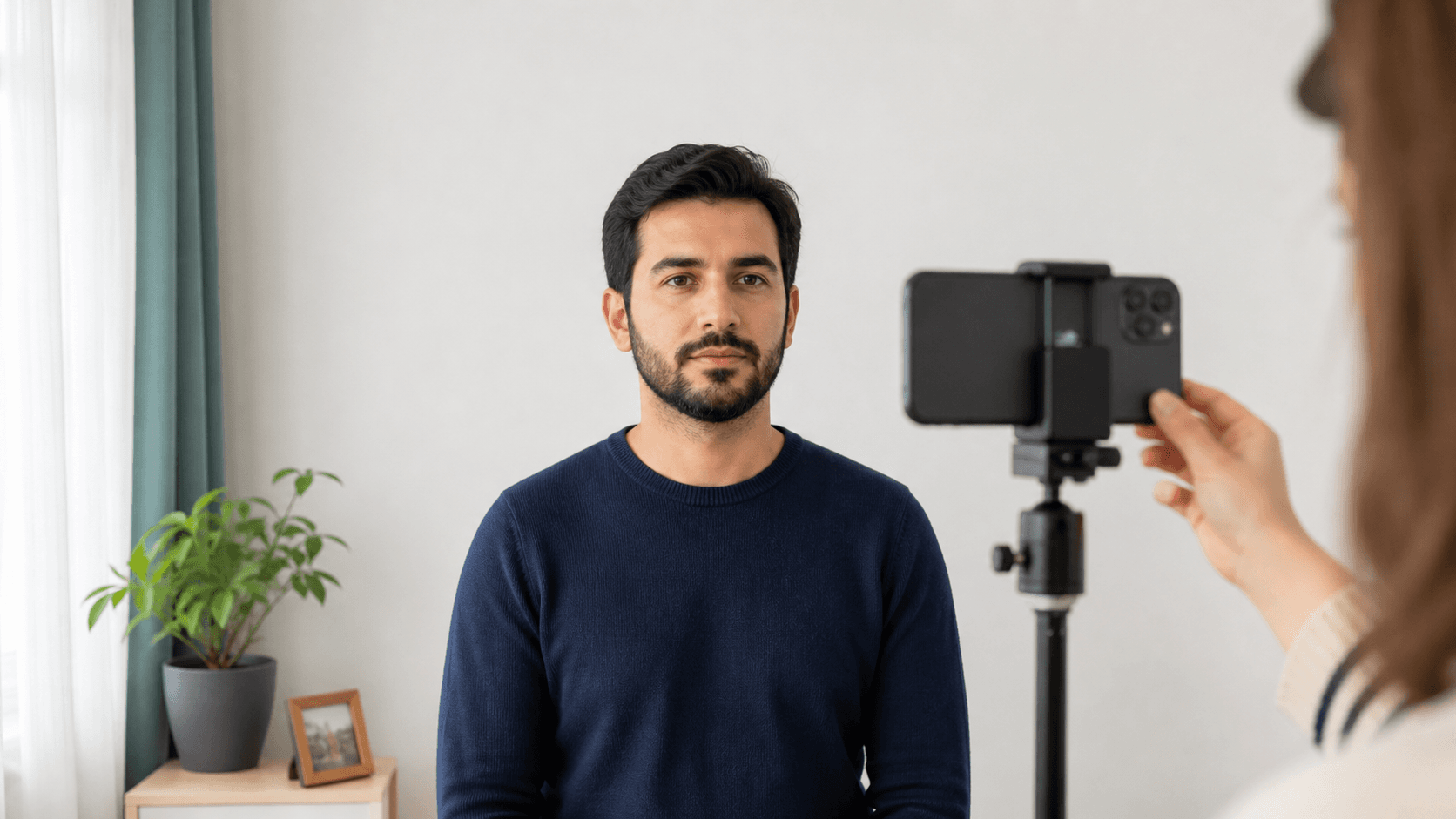 Evde beyaz duvarın önünde göz hizasına sabitlenmiş telefonla biyometrik fotoğraf çeken yetişkin